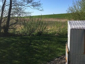 Une zone herbeuse avec un bâtiment au premier plan et une personne debout sur une colline à l’arrière-plan.