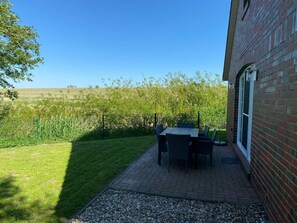 A patio with a table and chairs, a brick wall, and a view of a field. - Deichbrise - Deichbrise Vacation Home: A Relaxing Family Vacation in Greetsiel with (Krummhörn)