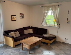 Un salon avec un canapé marron foncé, une table basse en bois et une fenêtre avec des rideaux.