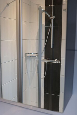 Eine begehbare Dusche mit Glaswänden, einem Chrom-Duschkopf und Bedienfeld.