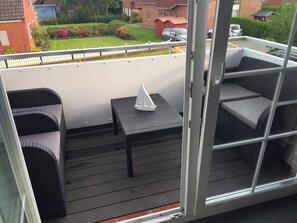 Ein Balkon mit Korbmöbeln, einem kleinen Tisch und Blick auf eine Wohngegend.