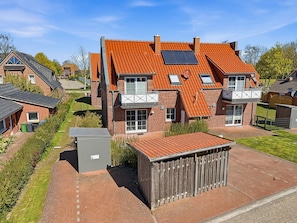 Ein zweigeschossiges Haus mit rotem Ziegeldach, einer kleinen angebauten Garage und einem umzäunten Garten.