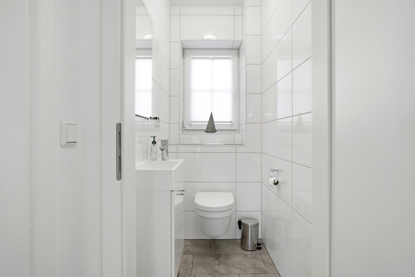 Ein kleines, modernes Badezimmer mit Toilette, Waschbecken und Fenster.