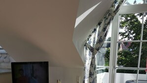 Una sala de estar con televisor, estanterías, una mesa de vidrio y vistas al exterior.