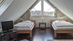 Un dormitorio moderno y pequeño en el ático, con dos camas, un escritorio y un televisor.
