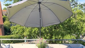 Un patio con una mesa lista para tomar té, mobiliario exterior y un paraguas grande.