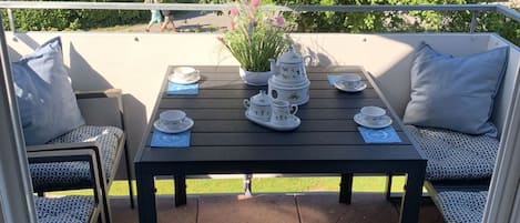Une terrasse avec une table préparée pour le thé, des sièges d’extérieur et un grand parasol.
