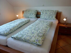 Un llit doble amb roba de llit estampada, una taula de nit amb una làmpada i un panell de fusta al capçal.