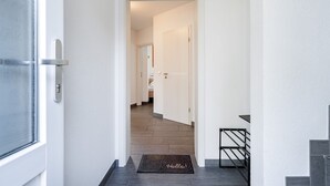 A hallway leading to a bedroom with a bed and a nightstand. - Löwenzahn - Apartment (70sqm) for 4 persons with terrace and sep. Guest WC (Krummhörn)