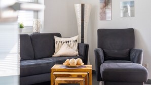 A modern living room with a dark grey sofa, a matching armchair, and a wooden coffee table with decorative items. - Löwenzahn - Apartment (70sqm) for 4 persons with terrace and sep. Guest WC (Krummhörn)