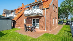 A two-story brick house with a balcony and a patio area with a table and chairs. - Löwenzahn - Apartment (70sqm) for 4 persons with terrace and sep. Guest WC (Krummhörn)