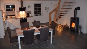 Eine moderne Küche mit weißen Schränken, ein Essbereich mit Tisch und Stühlen sowie eine Treppe zu einem Schlafzimmer im oberen Bereich.