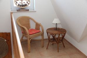 A corner room with a wicker chair and a small round table with a lamp.