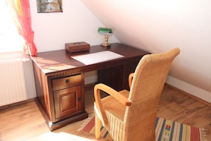 A wooden desk with a wicker chair, a radiator, a framed picture on the wall, and a lamp.