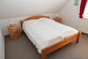 A single bed with a wooden frame and white bedding in a room with a sloped ceiling.