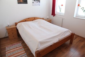 Ein Schlafzimmer mit einem hölzernen Bett, einem Nachttisch, einem Radiator und einem Fenster mit Vorhängen.