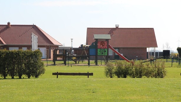 Un’area giochi con uno scivolo e strutture per arrampicata, circondata da un prato e un edificio con tetto in tegole rosse.