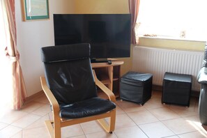 Ein Zimmer mit einem großen Flachbildfernseher, einem Holzstuhl, einem kleinen Tisch und einem schwarzen Hocker.