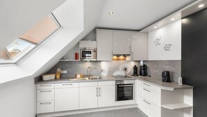 Una cocina moderna con armarios blancos, horno empotrado, microondas y cafetera.