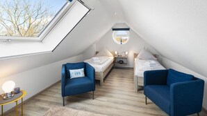 Un dormitorio moderno y pequeño en el ático, con tragaluces, dos camas, un escritorio y dos sillones azules.