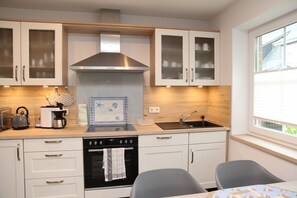 A modern kitchen with white cabinets, a stainless steel range hood, a built-in oven, a sink, and a window providing natural light. - Heimathaven - New first floor apartment (70sqm) with terrace for 4 persons centrally located (Krummhörn)