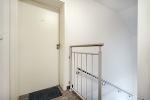 A white door with a metal handrail and a doorknob, a dark doormat, and a light-colored wall.