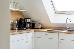 A kitchen with a wooden countertop, white cabinets, a coffee maker, a toaster, and a sink with a modern faucet.