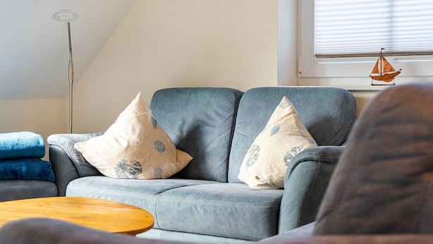 Una sala de estar con un sofá gris, dos almohadones decorativos, una mesa de centro de madera y un adorno de velero colgante.