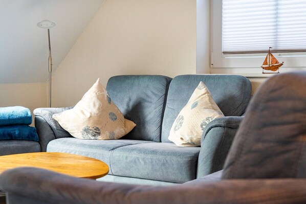 Una sala de estar con un sofá gris, dos almohadones decorativos, una mesa de centro de madera y un adorno de velero colgante.