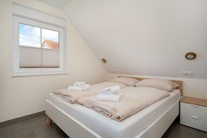 Ein Schlafzimmer mit Bett, Nachttisch, einem Fenster mit Jalousien und Blick auf ein Gebäude.