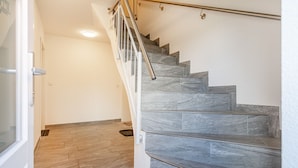 Una escalera de piedra gris con barandilla de metal, que conduce a una puerta.