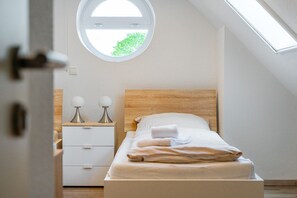 A bedroom with a wooden headboard, a round window, a bedside table with two lamps, and a neatly made bed.