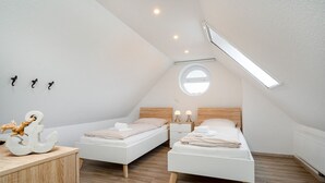 Un dormitorio ático moderno y luminoso con dos camas individuales, un aparador de madera y un tragaluz.