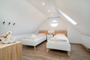 Un dormitorio ático moderno y luminoso con dos camas individuales, un aparador de madera y un tragaluz.