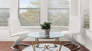 A modern room with a glass table and white chairs, a decorative plant, and large windows with blinds. - Modern 5 Bedrooms in SA Chef Kitchen, Game Lounge (San Antonio)