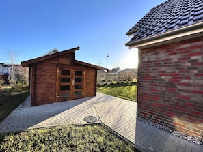 Eine Holzhütte mit Backsteinanbau, einem gepflasterten Weg und einer Rasenfläche.