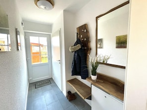 Ein Korridor mit einer weißen Tür, einer Holzbank, einem Kleiderhaken mit einem Fellaccessoire und einem Spiegel an der Wand.