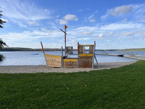A playground with a slide and climbing structures near a body of water. - Alleenhuus - Hochwertiges und Luxuriöses Ferienhaus Direkt am Wariner See (Warin)
