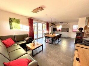 A modern living room with a sofa, coffee table, and dining area. There is a kitchen in the background with cabinets and a stove.