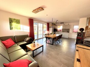 A modern living room with a sofa, coffee table, and dining area. There is a kitchen in the background with cabinets and a stove. - Alleenhuus - Hochwertiges und Luxuriöses Ferienhaus Direkt am Wariner See (Warin)