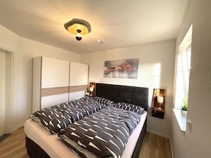 Un dormitorio moderno con una cama grande, una lámpara de techo, un cuadro y una ventana.