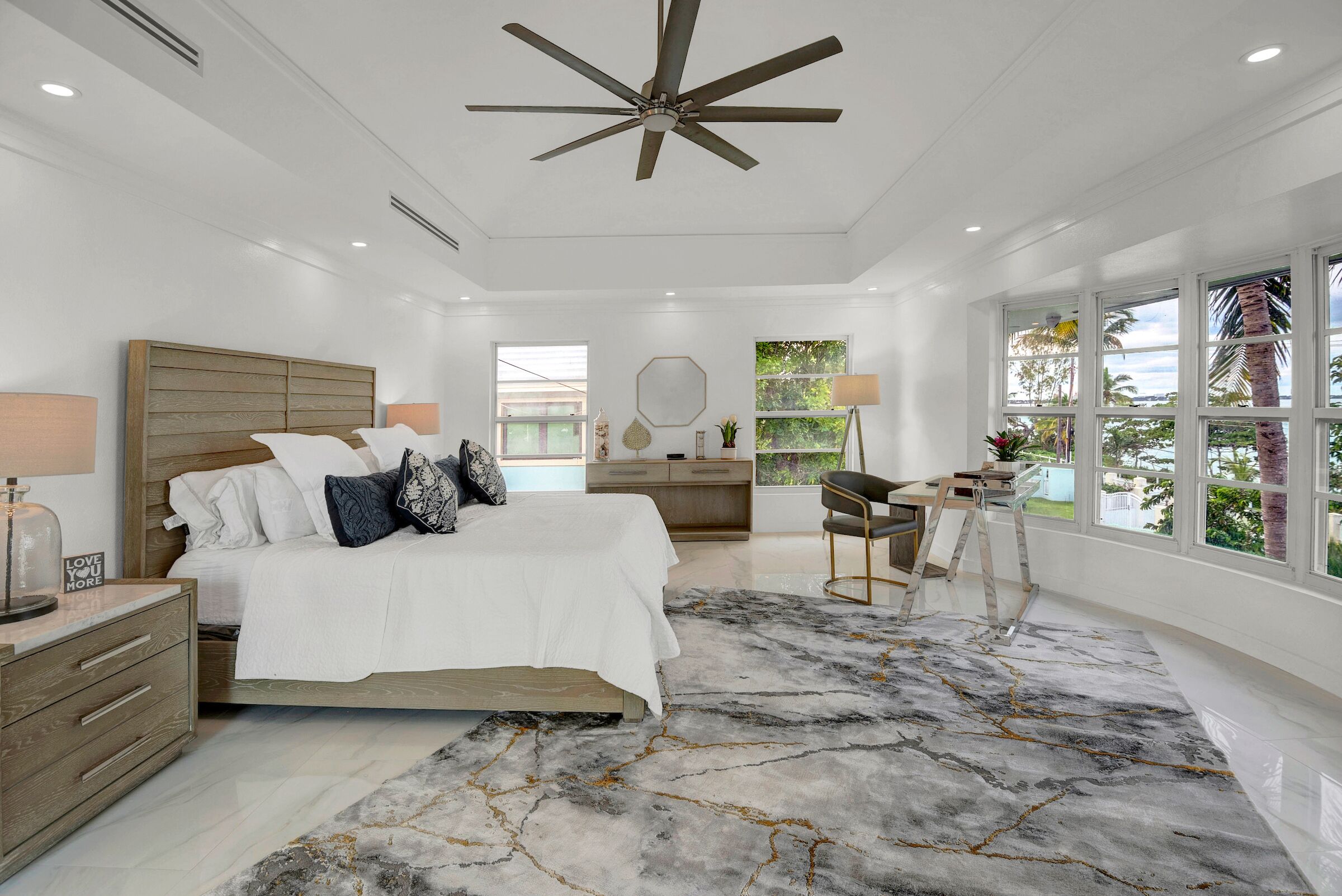 A spacious bedroom with a large bed, a ceiling fan, a desk, and a view of the outdoors.