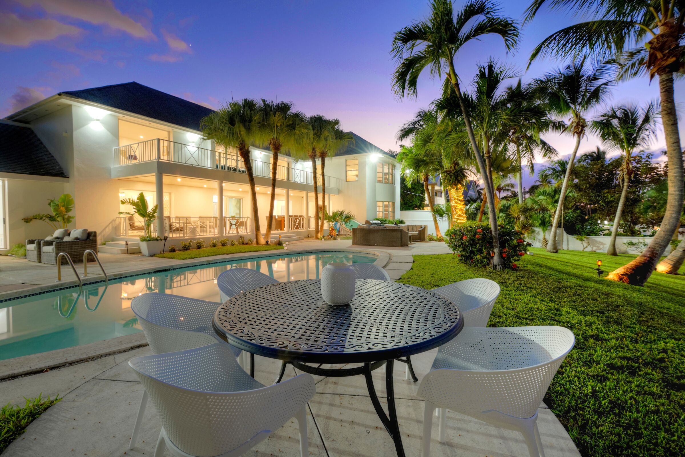 Een modern huis met een zwembad, terras en palmbomen.