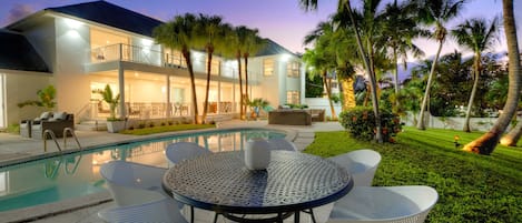 Een modern huis met een zwembad, terras en palmbomen.