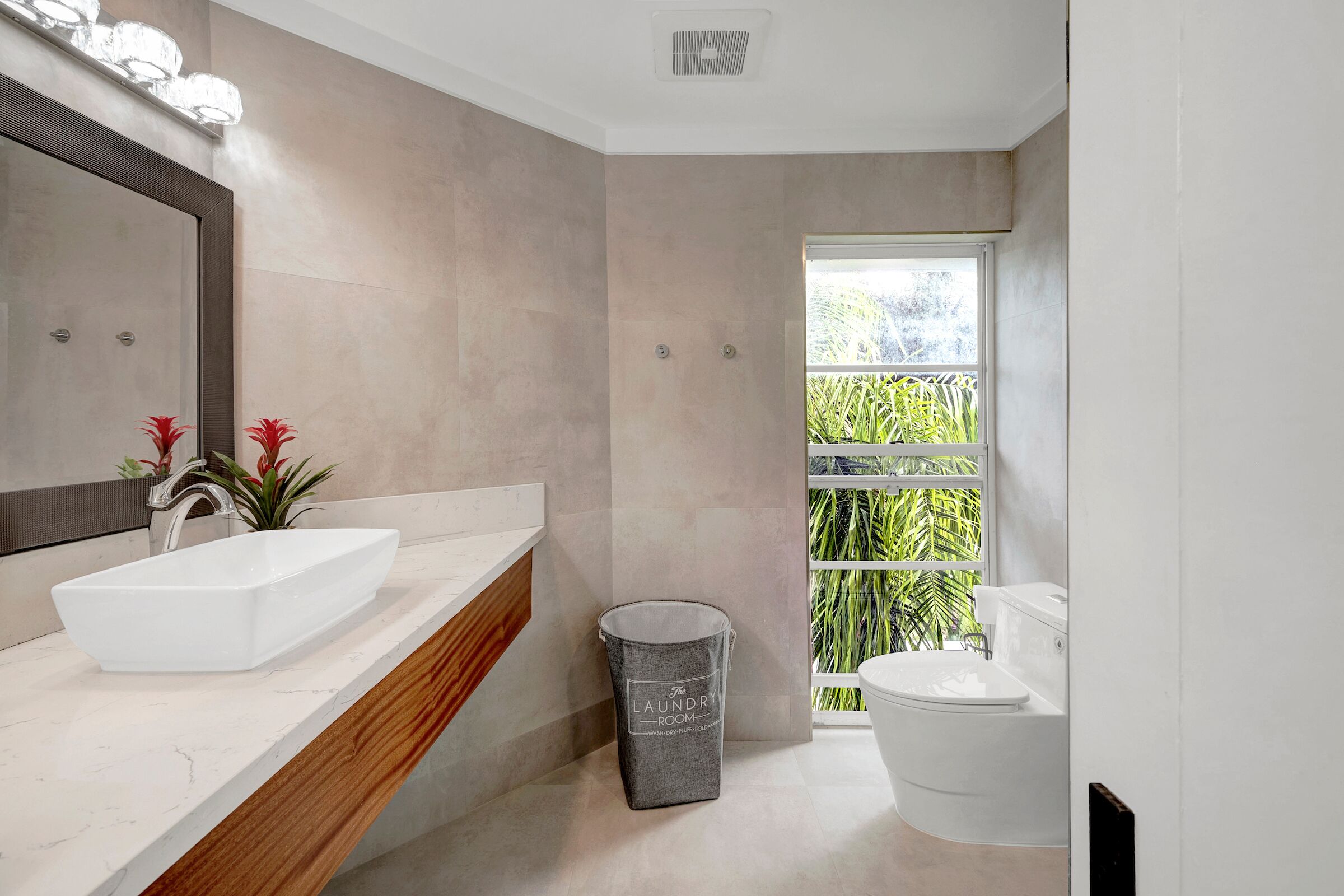 Ein modernes Badezimmer mit einem großen Spiegel, zwei Waschbecken, einer Toilette und einem Mülleimer.