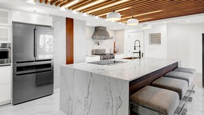 Cozinha moderna com uma ilha grande, eletrodomésticos de aço inoxidável e teto de madeira.