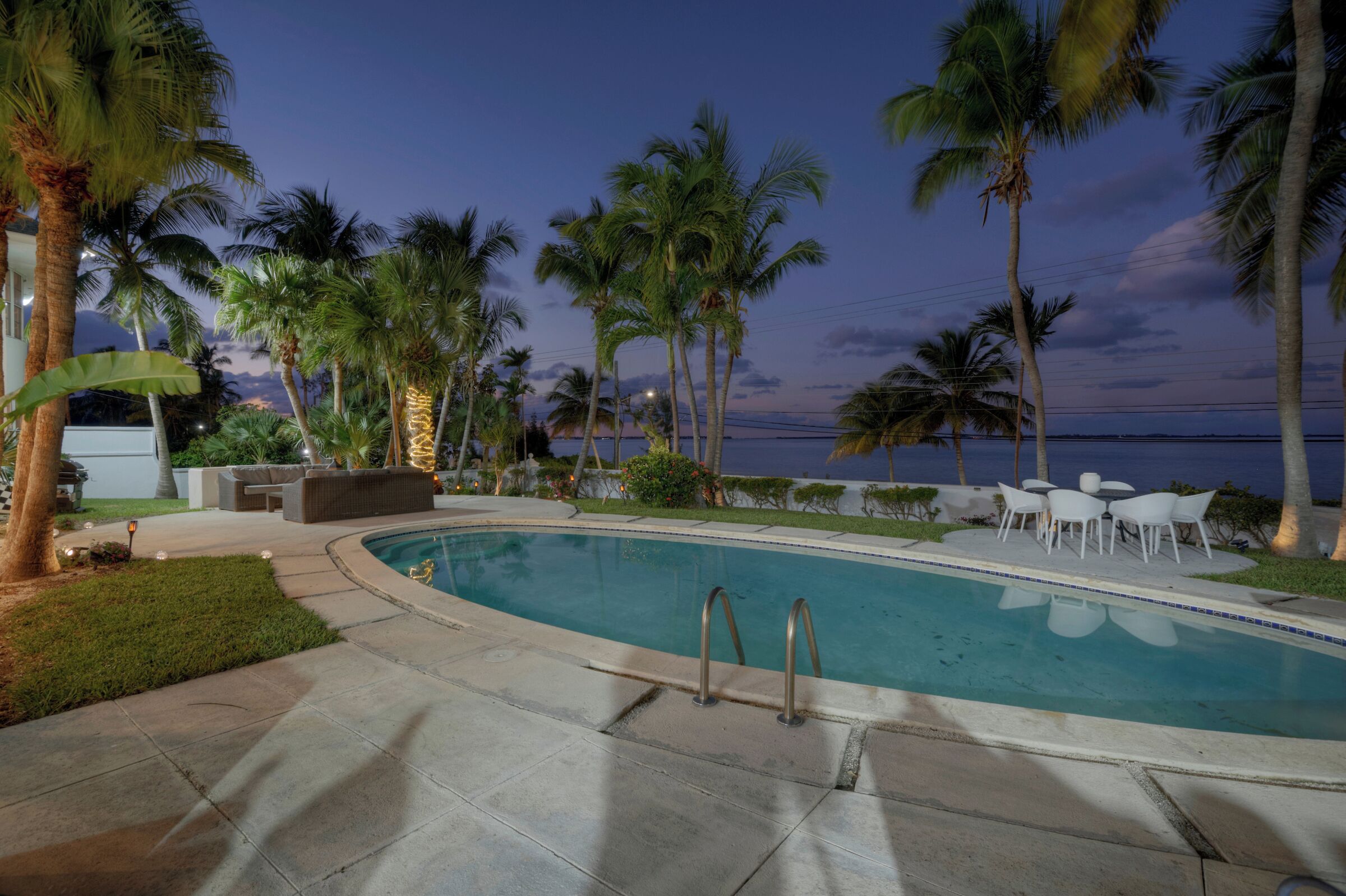 A pool area with palm trees, a lounge area, and a view of the ocean.