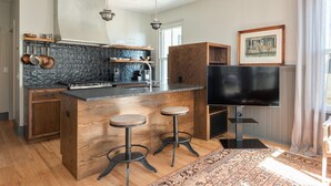 A modern kitchen with a central island, bar stools, a flat-screen TV, and a patterned rug. - Blacksmith Apartment | Lux Extended Stay in Belmont (Charlottesville)