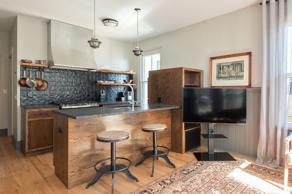 Une cuisine moderne dotée d’un îlot central, de tabourets de bar, d’un téléviseur à écran plat et d’un tapis à motifs.