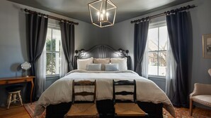 A bedroom with a large bed, two wooden chairs, a desk, and a mirror. - Blacksmith Apartment | Lux Extended Stay in Belmont (Charlottesville)